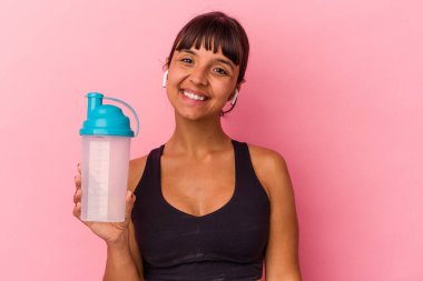 Genç melez kadın pembe arka planda izole edilmiş protein içeceği içiyor. Mutlu, güler yüzlü ve neşeli..