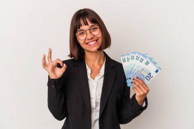 Genç melez iş kadını elinde banknotlarla beyaz arka planda izole edilmiş neşeli ve kendinden emin bir şekilde iyi niyet gösteriyor..