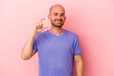 Kafkasyalı genç kel adam pembe arka planda izole edilmiş. Elinde parmakları olan, gülümseyen ve kendinden emin bir şey var..