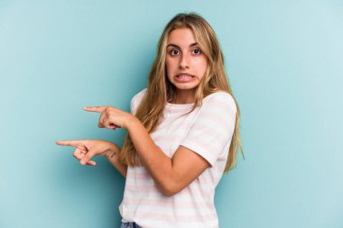 Mavi arka planda izole edilmiş beyaz, genç bir kadın işaret parmağıyla fotokopi alanını işaret ederek şok oldu..