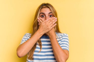 Sarışın, sarı arka planda izole edilmiş genç bir kadın elleriyle ağzını kapatırken şok oldu..
