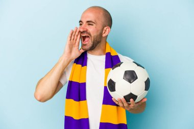 Mavi arka planda izole edilmiş atkı takan genç ve kel bir adam bağırıyor ve avuç içini açık tutuyor..