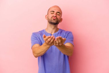Beyaz tenli kel bir adam pembe arka planda izole edilmiş dudaklar kıvrılmış ve hava öpücüğü vermek için avuç içleri tutulmuş..