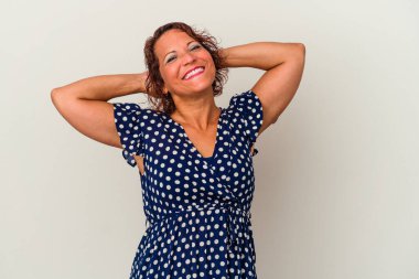 Beyaz arka planda izole edilmiş orta yaşlı Latin bir kadın kendini güvende hissediyor, elleri başının arkasında..