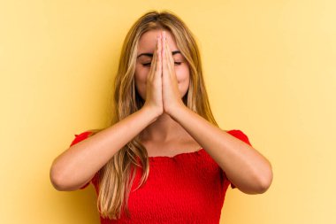 Sarışın, sarı arka planda izole edilmiş genç, ağzı yakınken el ele dua eden, kendinden emin bir kadın..