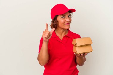 Burgerleri alan orta yaşlı bir kadın beyaz arka planda bir numarayı parmağıyla gösteriyor..