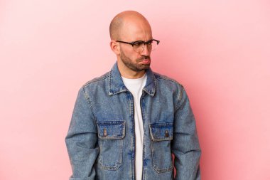 Pembe arka planda izole edilmiş beyaz, kel genç bir adam tekrarlanan bir görevden yoruldu..