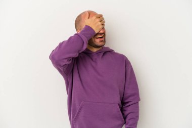 Beyaz arka planda soyutlanmış genç kel bir adam elleriyle gözlerini kapatıyor, gülümseyerek bir sürpriz bekliyor..