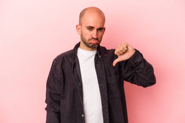 Pembe arka planda izole edilmiş genç, beyaz, kel adam baş parmağını aşağı gösteriyor, hayal kırıklığı konsepti..