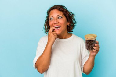 Orta yaşlı Latin bir kadın elinde kahve kavanozu tutuyordu. Mavi arka planda izole edilmişti. Bir şeyin fotokopi odasına baktığını sanıyordu..
