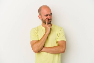 Genç kel adam beyaz arka planda izole edilmiş şüpheli ve şüpheci bir ifadeyle yana bakıyor..