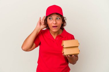 Beyaz arka planda izole edilmiş burgerleri alan orta yaşlı bir teslimatçı kadın bir dedikoduyu dinlemeye çalışıyor..