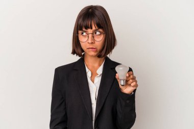 Beyaz arka planda izole edilmiş ampulü tutan genç, melez bir iş kadını kafası karışmış ve kendinden emin değil..