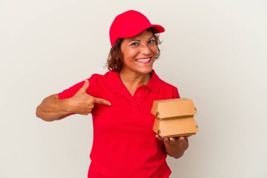 Burgerciyi beyaz arka planda izole eden orta yaşlı bir kadın gömlek fotokopi alanını işaret ediyor, gururlu ve kendinden emin.