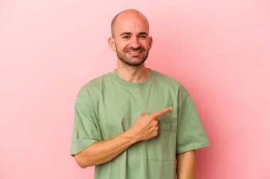 Pembe arka planda izole edilmiş beyaz kel bir adam gülümsüyor ve boş alanda bir şeyler gösteriyor..