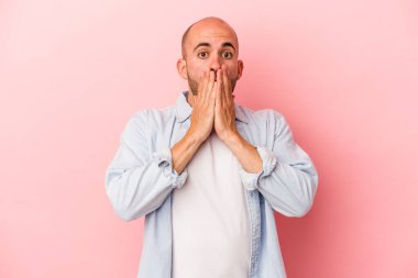 Pembe arka planda soyutlanmış beyaz kel bir adam elleriyle ağzını kapatırken şok oldu..