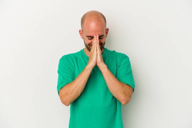Beyaz arka planda izole olmuş genç kel bir adam. El ele tutuşup, ağzının kenarında dua ediyor. Kendine güveniyor..