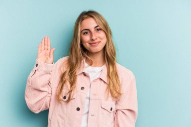 Mavi arka planda izole edilmiş beyaz, genç bir kadın gülümseyerek beş numarayı parmaklarıyla gösteriyor..