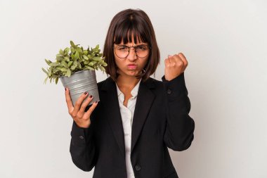 Beyaz arka planda bir bitki tutan genç melez iş kadını kameraya yumruk gösteriyor, agresif yüz ifadesi..