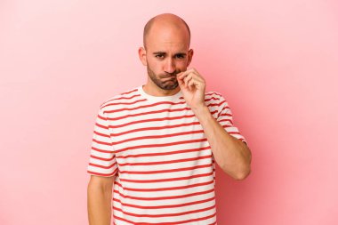 Genç beyaz kel adam pembe arka planda izole edilmiş ve parmakları dudaklarında bir sır saklıyor..