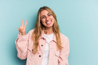 Kafkasyalı genç sarışın kadın mavi arka planda izole edilmiş neşeli ve kaygısız parmaklarıyla barış sembolü gösteriyor..