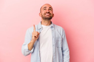 Pembe arka planda soyutlanmış beyaz saçlı genç bir adam iki parmağı da boş bir alan gösteriyor..