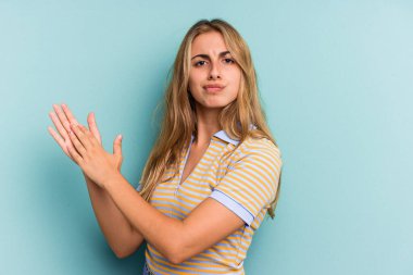 Mavi arka planda izole edilmiş genç beyaz kadın enerjik ve rahat hissediyor, ellerini ovuşturuyor, kendinden emin..