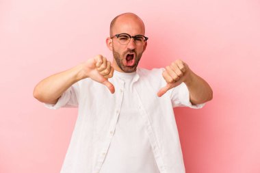 Pembe arka planda soyutlanmış genç, beyaz kel bir adam baş parmağını aşağı gösteriyor ve hoşlanmadığını ifade ediyor..