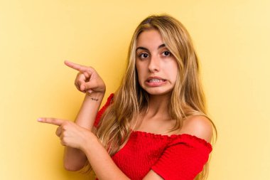 Sarı arka planda izole edilmiş beyaz, genç bir kadın işaret parmağıyla fotokopi alanını işaret ederek şok oldu..