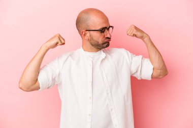 Pembe arka planda yalıtılmış genç, beyaz, kel bir adam kollarıyla güçlü bir hareket gösteriyor, kadınsı gücün sembolü.