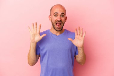 Genç beyaz kel adam pembe arka planda izole edilmiş. Hoş bir sürpriz bekliyor. Heyecanlı ve el kaldırıyor..