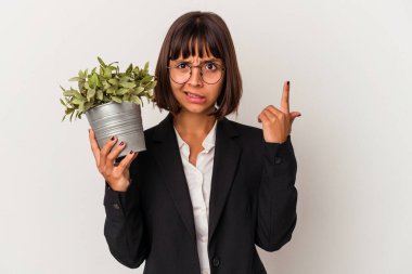Beyaz arka planda bir bitki tutan genç melez iş kadını işaret parmağıyla yaptığı hayal kırıklığı jestini gösteriyor..