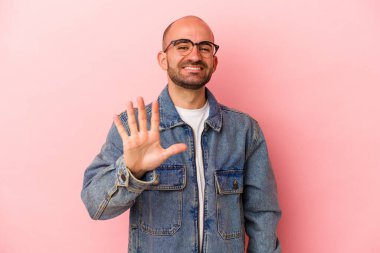 Kafkasyalı kel adam pembe arka planda izole edilmiş gülümseyen beş numarayı parmaklarıyla gösteriyor..