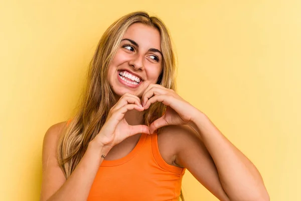 Young Caucasian Blonde Woman Isolated Yellow Background Smiling Showing Heart — Stock Photo, Image
