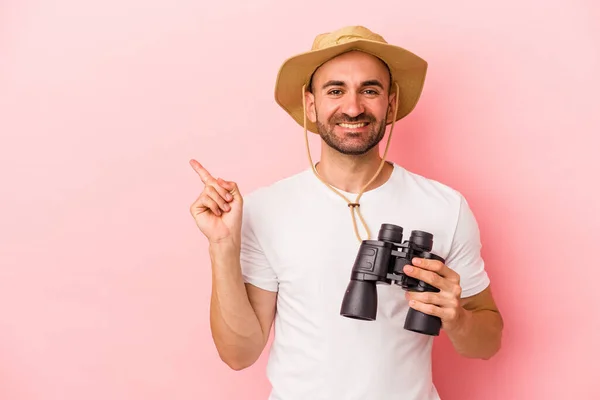 Jovem Caucasiano Careca Segurando Binóculos Isolados Fundo Rosa Sorrindo Apontando — Fotografia de Stock