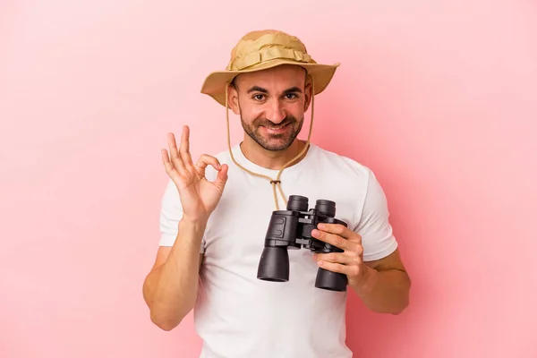 年轻的高加索秃头男子拿着双筒望远镜 背景是粉红色的 开朗而自信地摆出一副不错的姿势 — 图库照片