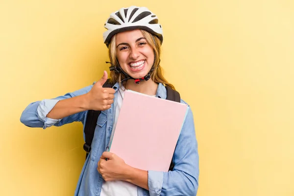 若いですCaucasian学生女性身に着けていますAバイクヘルメット隔離上の黄色の背景笑顔と上げ親指アップ — ストック写真