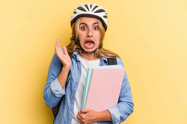若いですCaucasian学生女性身に着けていますAバイクヘルメット隔離上の黄色の背景驚きとショック — ストック写真