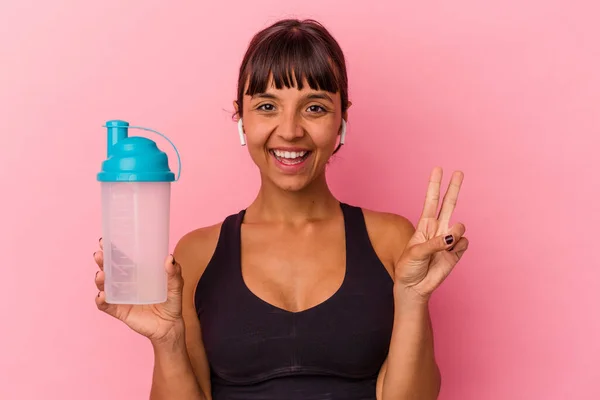 ピンクの背景に単離されたタンパク質シェイクを飲む若い混合レース女性は指で2番を示す — ストック写真
