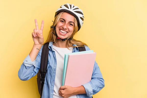 若いですCaucasian学生女性身に着けていますAバイクヘルメット絶縁上の黄色の背景ショーナンバー2とともに指 — ストック写真