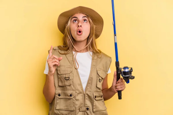 Young Caucasian Blonde Fisherwoman Holding Rod Isolated Yellow Background Pointing — Stock Photo, Image