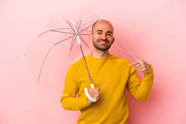 ピンクの背景に孤立した傘を手でシャツのコピースペースを指している若い白人のはげ男 誇りと自信 — ストック写真