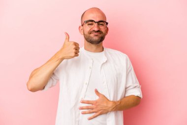 Beyaz tenli kel adam pembe arka planda izole edilmiş karnına dokunuyor, nazikçe gülümsüyor, yemek yiyor ve tatmin oluyor..