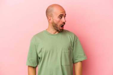 Genç beyaz kel adam pembe arka planda izole edilmiş. Gördüğü bir şey yüzünden şoka uğruyor..
