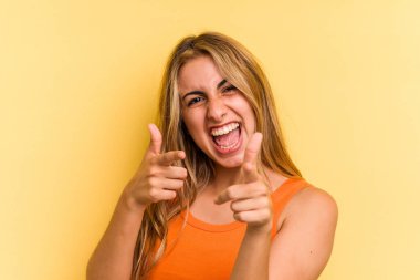 Sarışın, sarı arka planda izole edilmiş genç bir kadın. Önü işaret eden neşeli gülücükler..