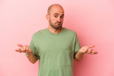 Kafkasyalı genç kel adam pembe arka planda izole edilmiş şüpheli ve sorgulama sırasında omuz silkiyor..