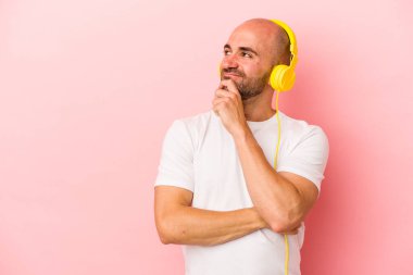 Pembe arka planda izole edilmiş müzik dinleyen beyaz, kel bir adam şüpheli ve şüpheci bir ifadeyle yan yana bakıyor..