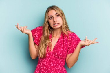 Kafkasyalı genç sarışın kadın mavi arka planda izole edilmiş sorgulama sırasında omuz silkiyor ve kuşkulanıyor..