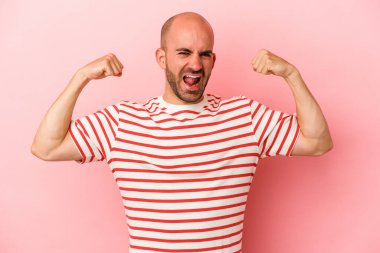 Pembe arka planda yalıtılmış genç, beyaz, kel bir adam kollarıyla güçlü bir hareket gösteriyor, kadınsı gücün sembolü.