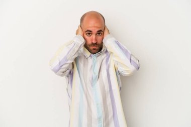 Genç kel adam beyaz arka planda izole edilmiş kulakları elleriyle kapatıyor yüksek sesli sesler duymamaya çalışıyor..